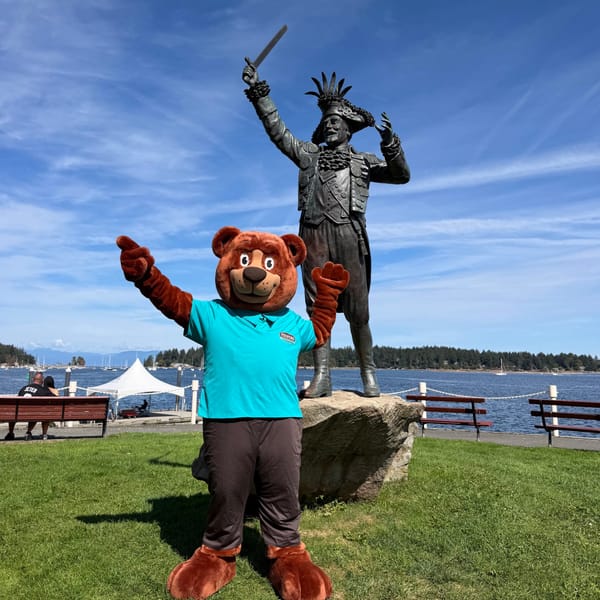 The Tedford bear mascot waving beside a statue on the Nanaimo waterfront