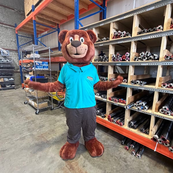 The Tedford bear mascot in front of shelves of garage door springs in the Tedford shop