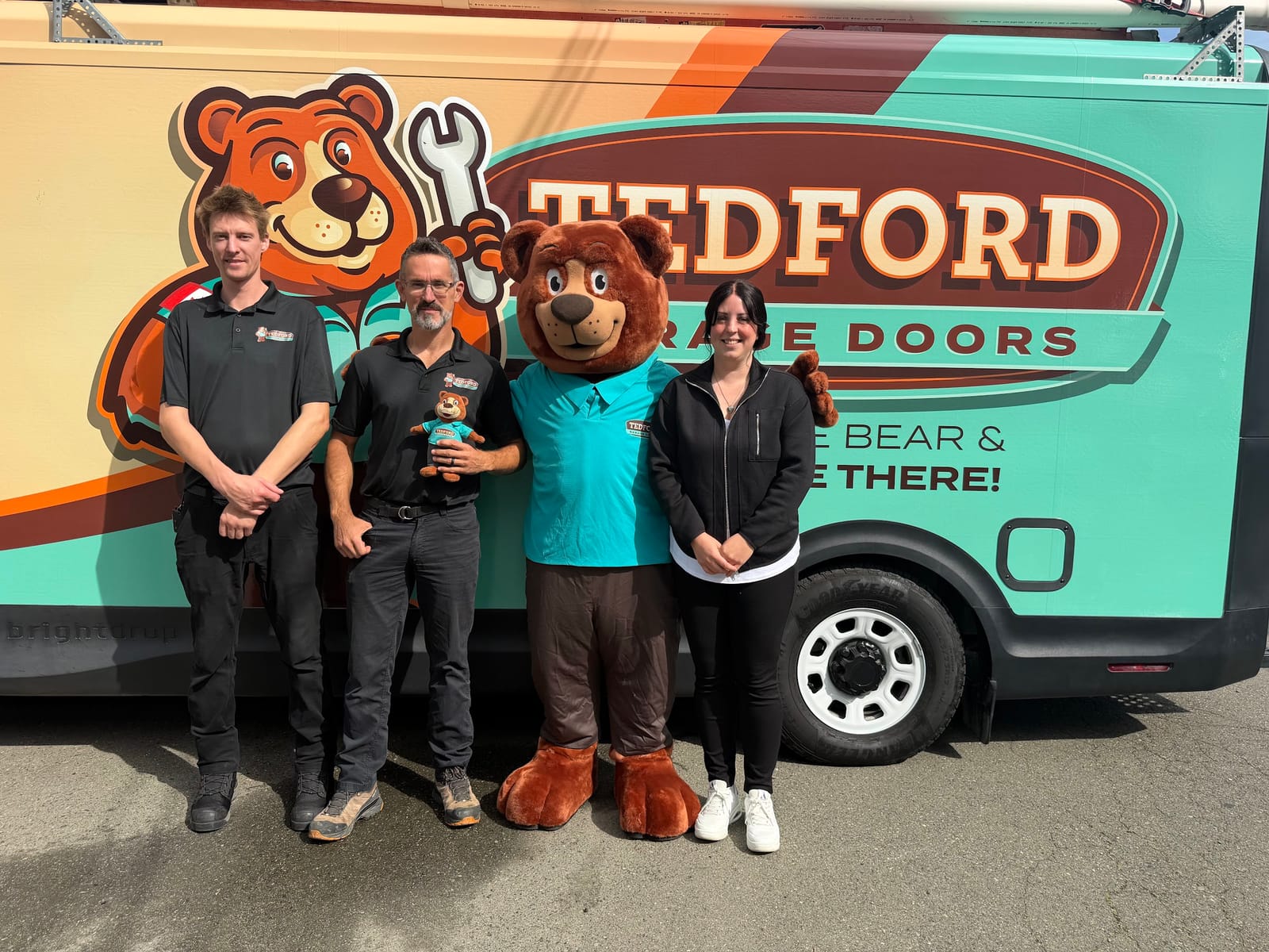 Three members of the Tedford Garage Doors Nanaimo team with the Tedford bear mascot in front of a Tedford service van